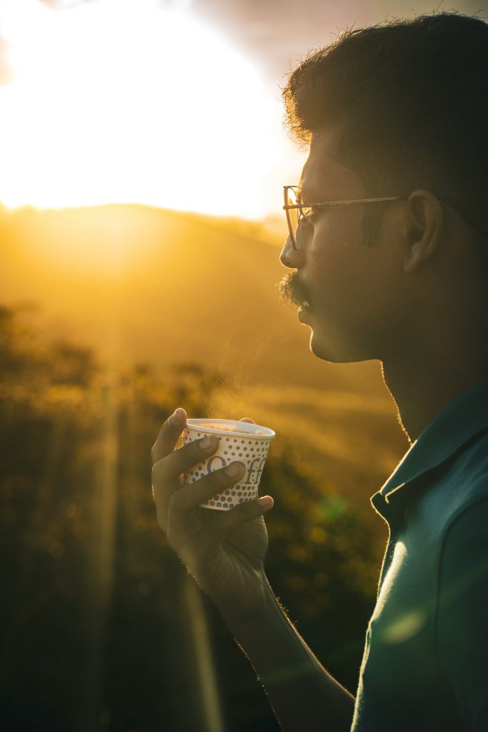 Munnar Man Holds a Tea Cup to Drink at Sunrise, Photo by Nandhu Kumar, Unsplash